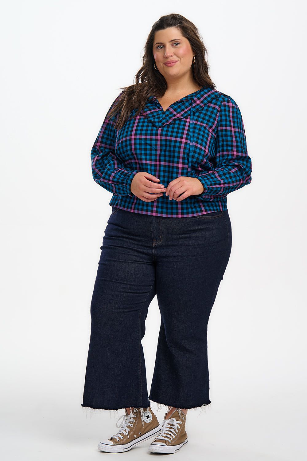 Woman wearing a blue and pink plaid shirt with dark jeans on a white background