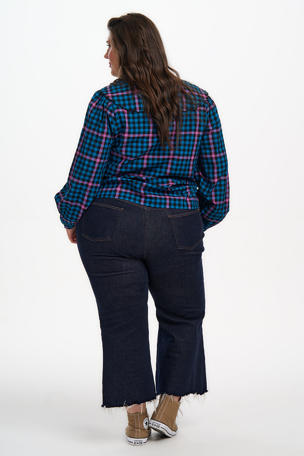 Person wearing a plaid shirt and dark jeans on a white background