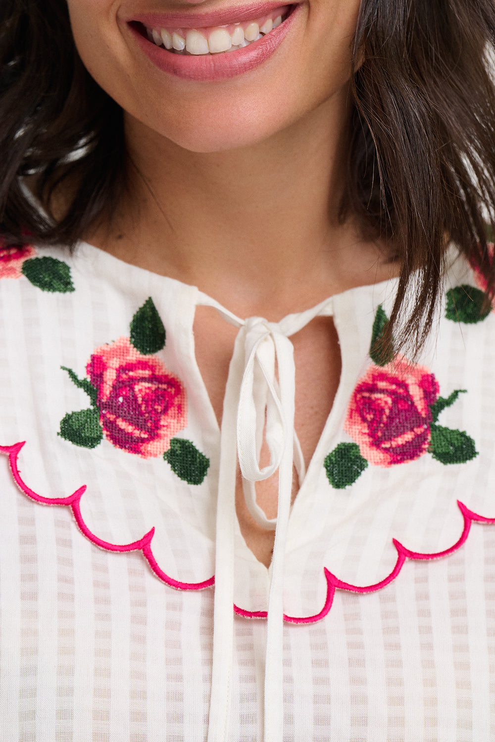 Close-up of a white blouse with pink floral embroidery and scalloped edge.