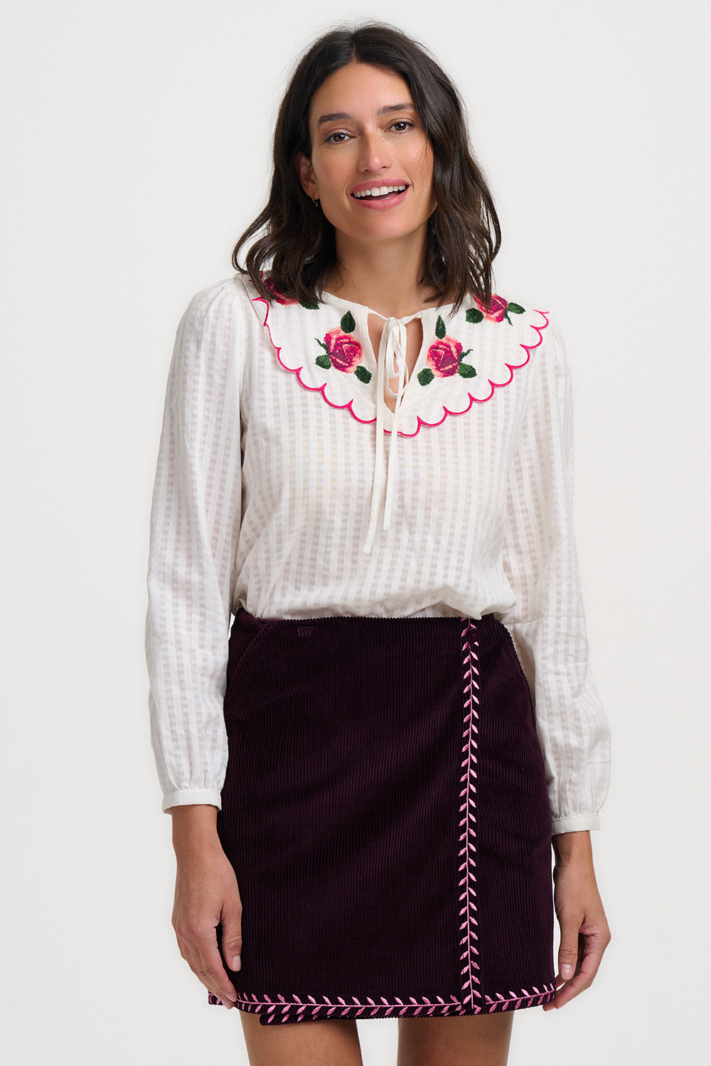 Woman wearing a white blouse with floral embroidery and a black skirt with decorative stitching on a white background