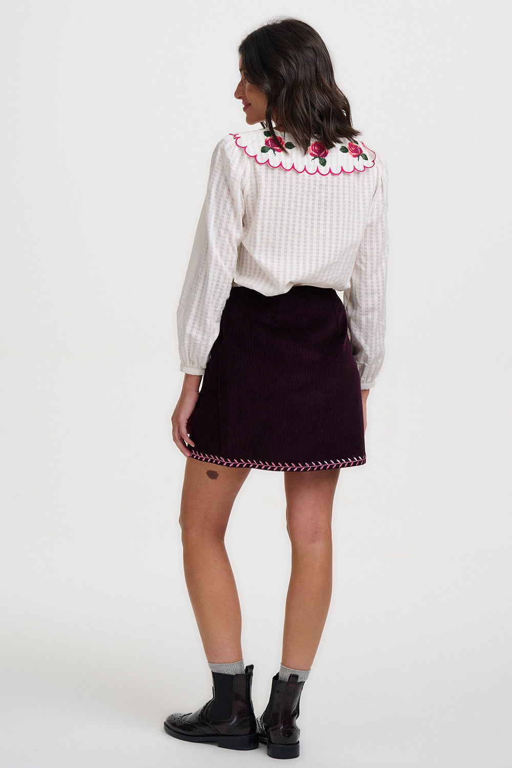 Woman wearing a white blouse with floral embroidery and a dark skirt on a white background