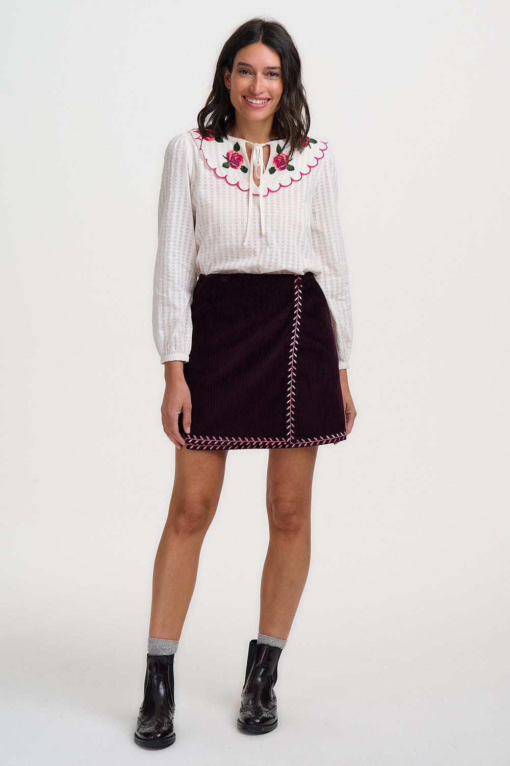 Woman wearing a white blouse with red embroidery and a dark skirt with red stitching on a white background
