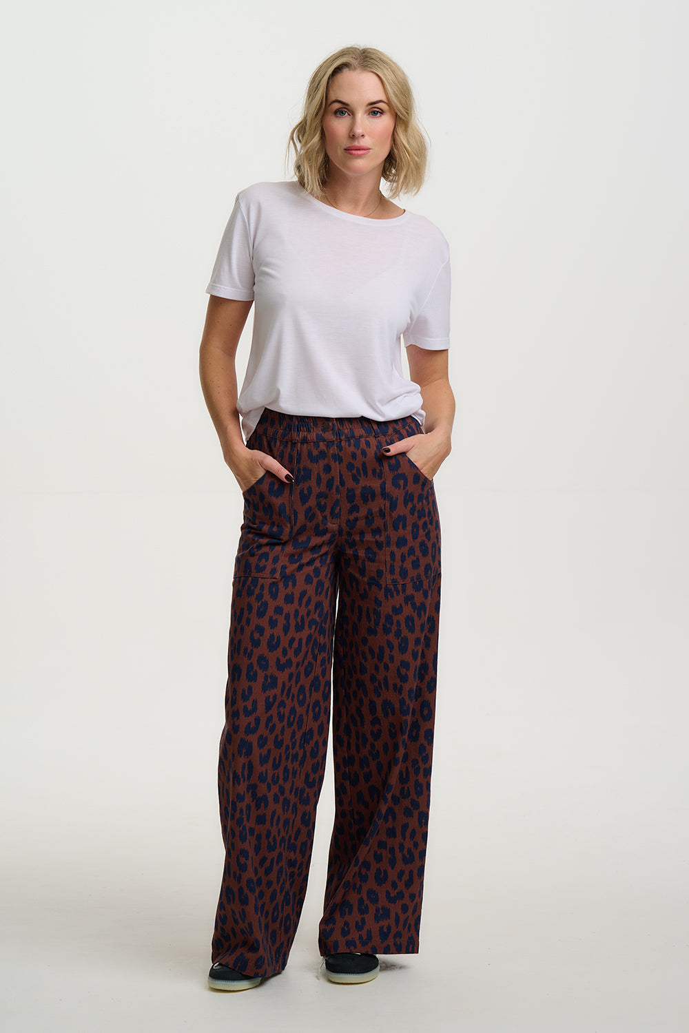 Woman wearing a white t-shirt and patterned pants on a plain background