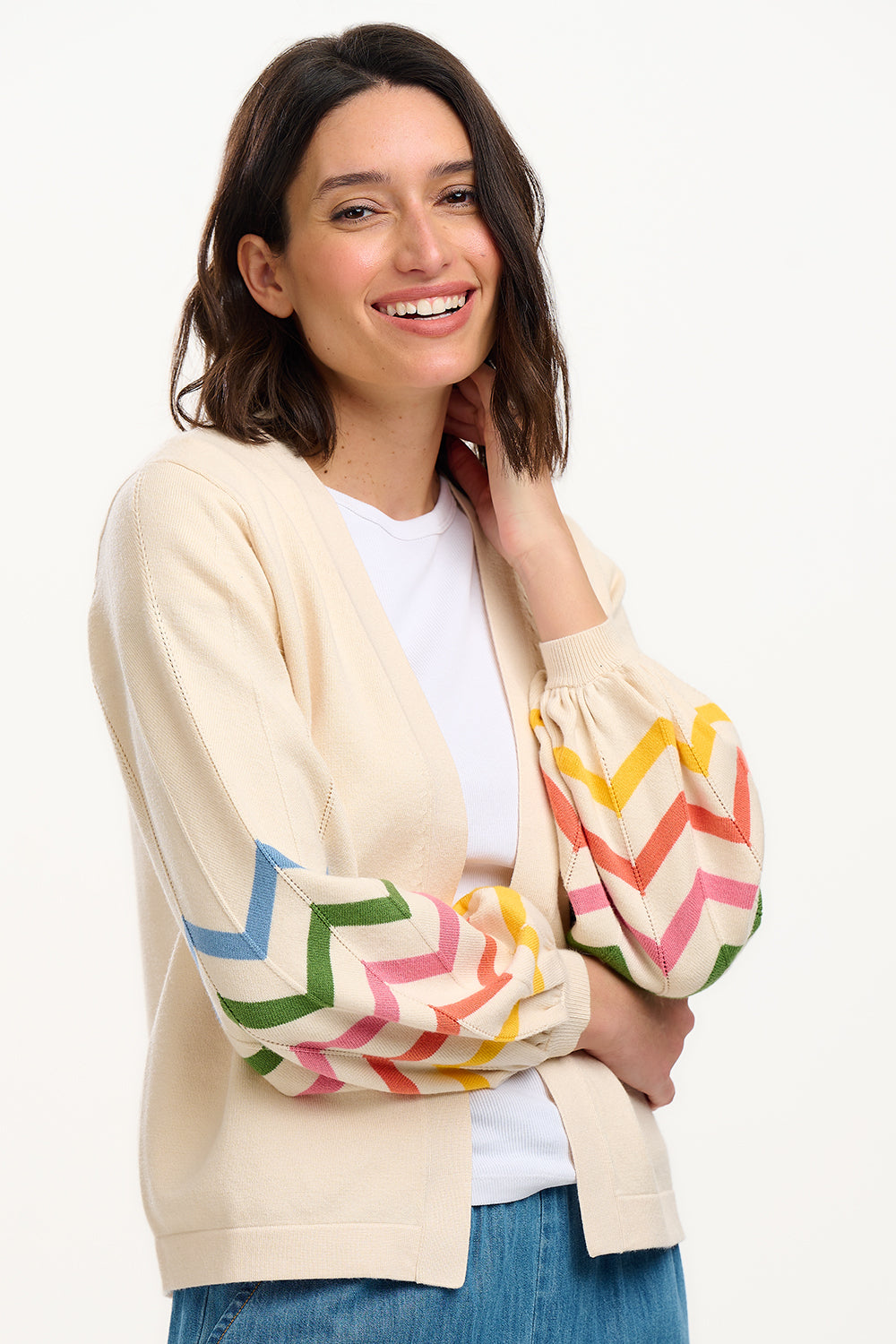 A woman smiling and wearing an off-white cardigan with rainbow-colored chevron stripes on the sleeves.