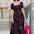 Woman in a patterned dress holding a pink bag outside a building.