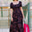 Woman in a patterned dress holding a pink bag outside a building.