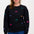 A woman wearing a black sweatshirt with multicoloured embroidered dinosaurs