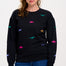 A woman wearing a black sweatshirt with multicoloured embroidered dinosaurs