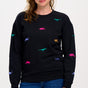 A woman wearing a black sweatshirt with multicoloured embroidered dinosaurs