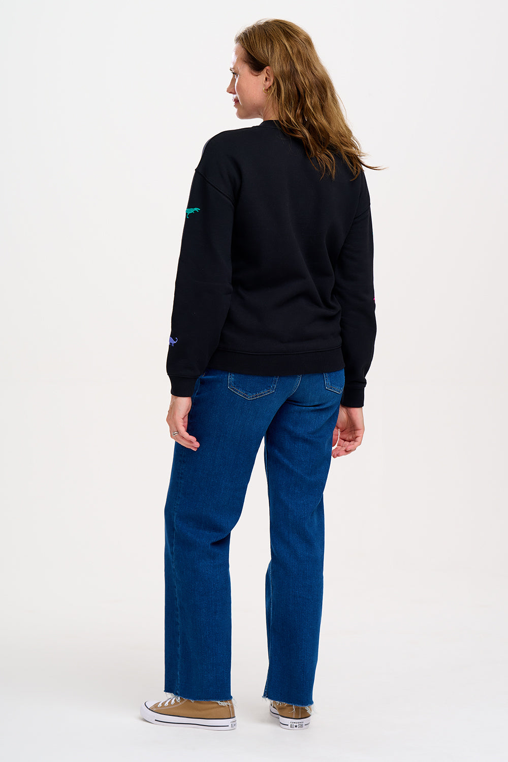 A woman wearing a black sweatshirt with multicoloured embroidered dinosaurs