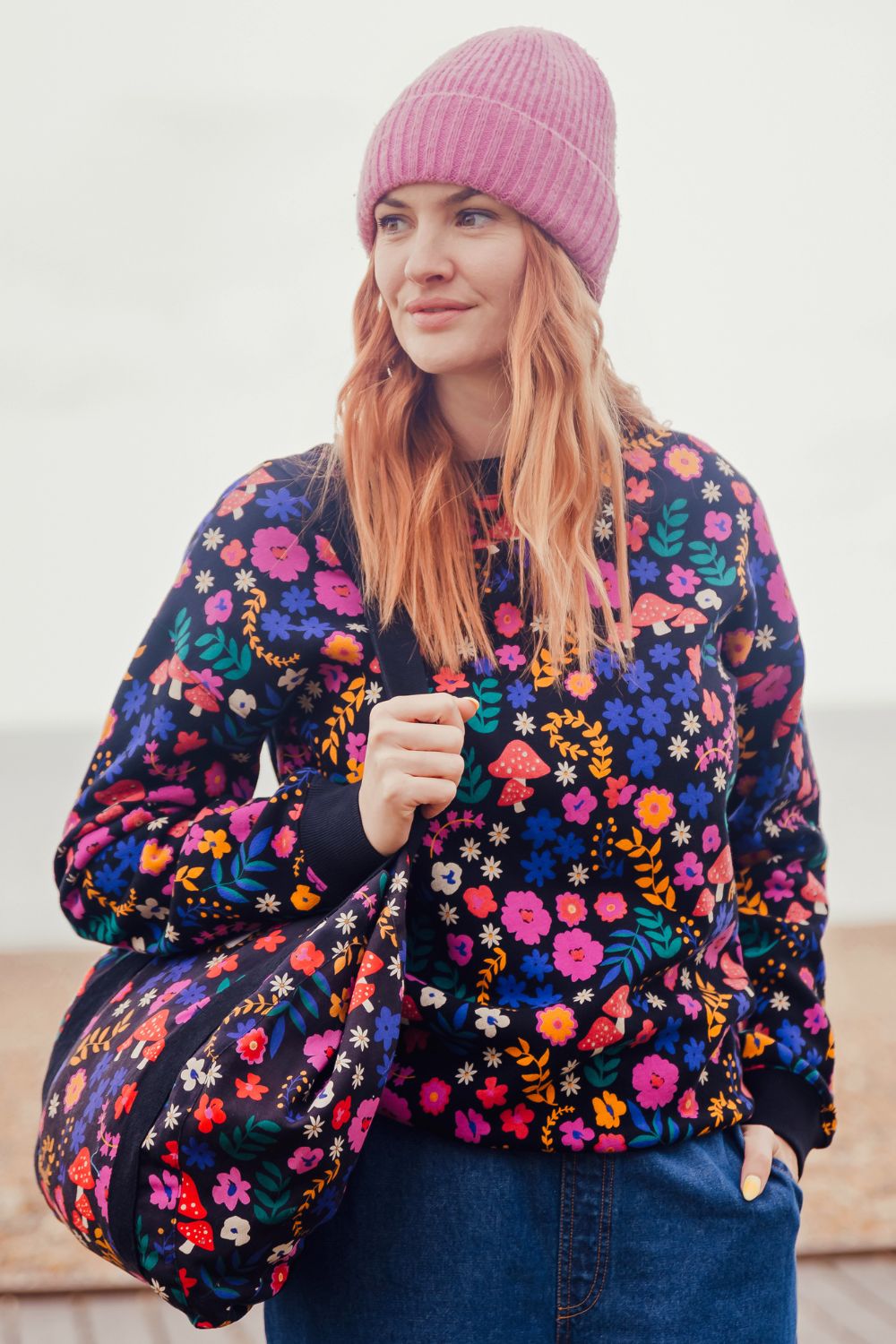 Woman wearing a colorful floral jacket and pink beanie against a white background