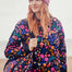 Woman wearing a colorful floral jacket and pink beanie against a white background