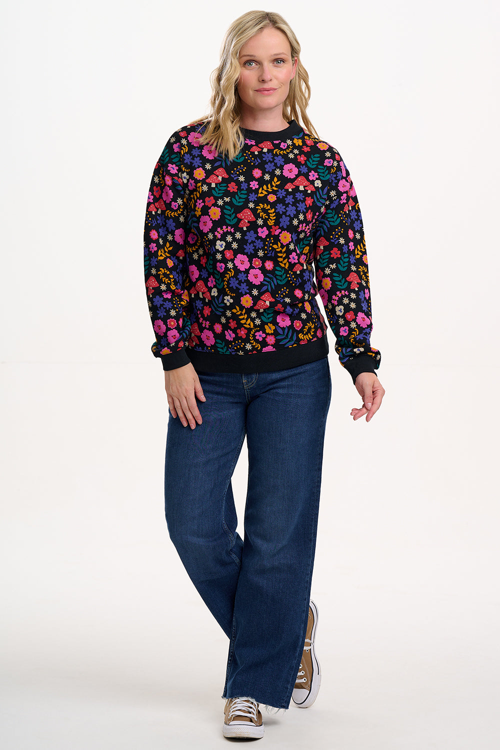 Woman wearing a colorful floral sweater and blue jeans on a white background