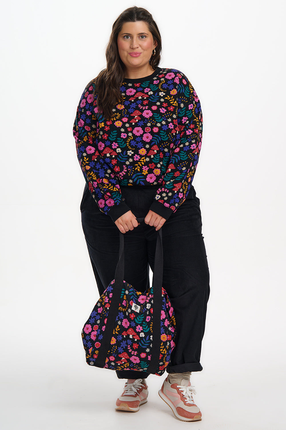 Woman wearing a colorful floral sweater and pants with a matching bag on a white background