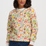 A woman wearing a long-sleeve crewneck sweatshirt with a colorful forest and deer pattern, paired with dark blue jeans, against a light gray studio background.