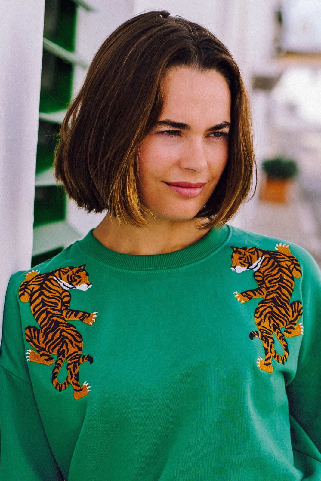 A woman wearing a green sweatshirt with embroidered tigers climbing the shoulders.