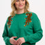 A woman wearing a green sweatshirt with embroidered tigers climbing the shoulders.