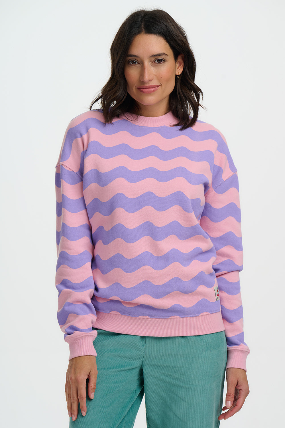 Woman wearing a pink and purple striped sweater with teal pants on a white background