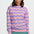 Woman wearing a pink and purple striped sweater with teal pants on a white background
