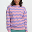 Woman wearing a pink and purple striped sweater with teal pants on a white background