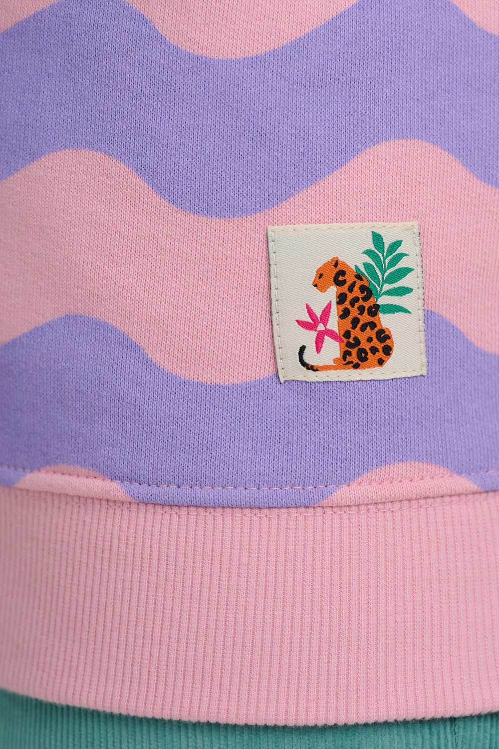 Close-up of a sweater with a colorful patch featuring a leopard design on a pink and purple striped background.