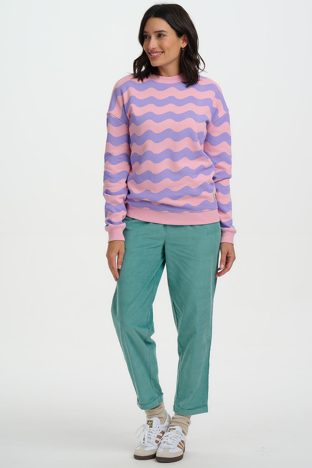 Woman wearing a pink and purple striped sweater with teal pants on a white background