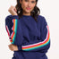 A navy sweatshirt with rainbow trim on the sleeves, displayed on a model against a white background.