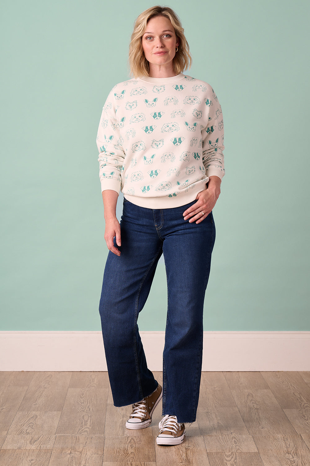 A woman wearing an off-white sweatshirt with a pattern of sketched dog faces in green.