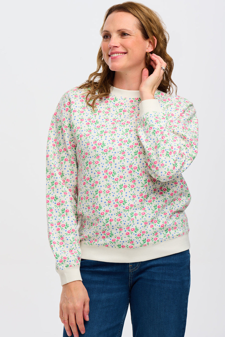 A woman wearing an off-white sweatshirt with a small floral print, crew neck, and ribbed cuffs.