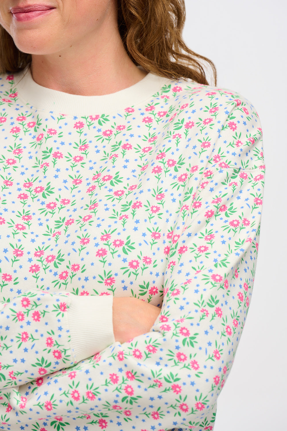 A woman wearing an off-white sweatshirt with a small floral print, crew neck, and ribbed cuffs.