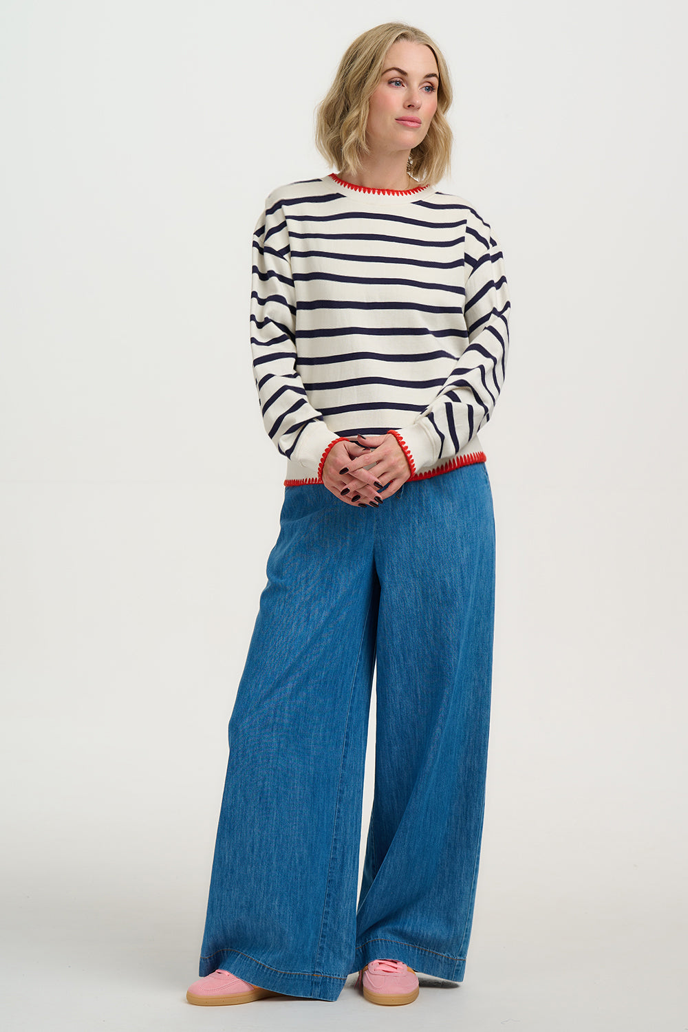 Woman wearing a striped sweater and blue wide-leg pants on a white background