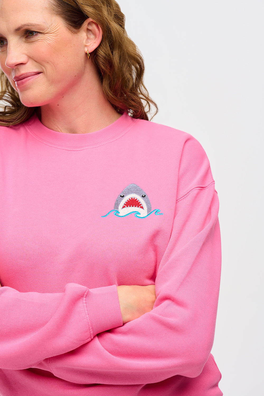 A woman wearing a pink sweatshirt with a shark embroidery on the chest.