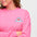 A woman wearing a pink sweatshirt with a shark embroidery on the chest.