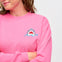 A woman wearing a pink sweatshirt with a shark embroidery on the chest.