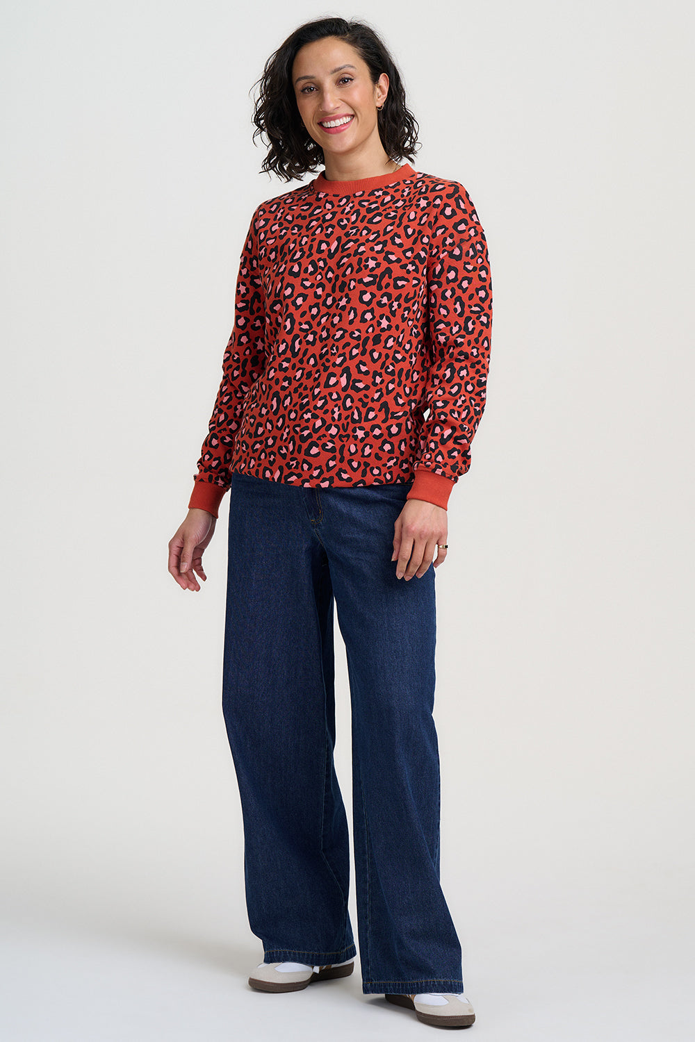 Woman wearing a red leopard print sweater and blue pants on a white background