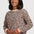 A woman wearing a beige crewneck sweatshirt with a brown and black leopard print pattern, featuring pink and white striped ribbed cuffs, set against a plain light gray background.