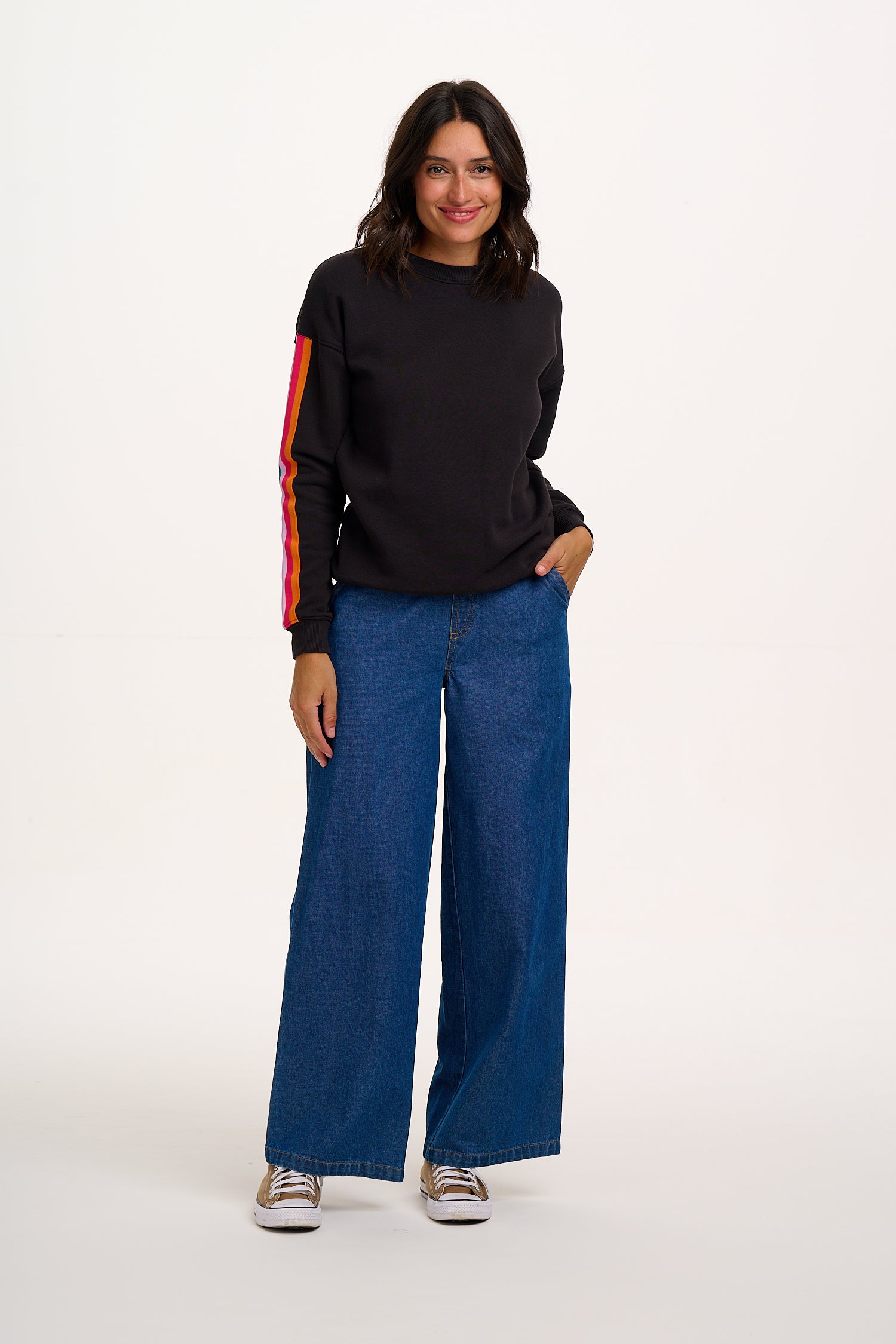 Woman wearing a black sweater with red sleeves and blue jeans on a white background