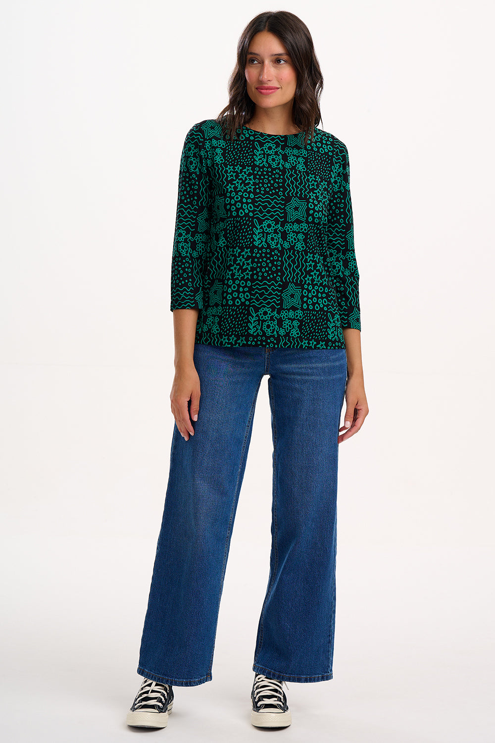 Woman wearing a green patterned top and blue jeans on a white background