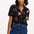 A woman smiling and wearing a short-sleeved black shirt with a rainbow parrots and flowers print, paired with blue jeans.