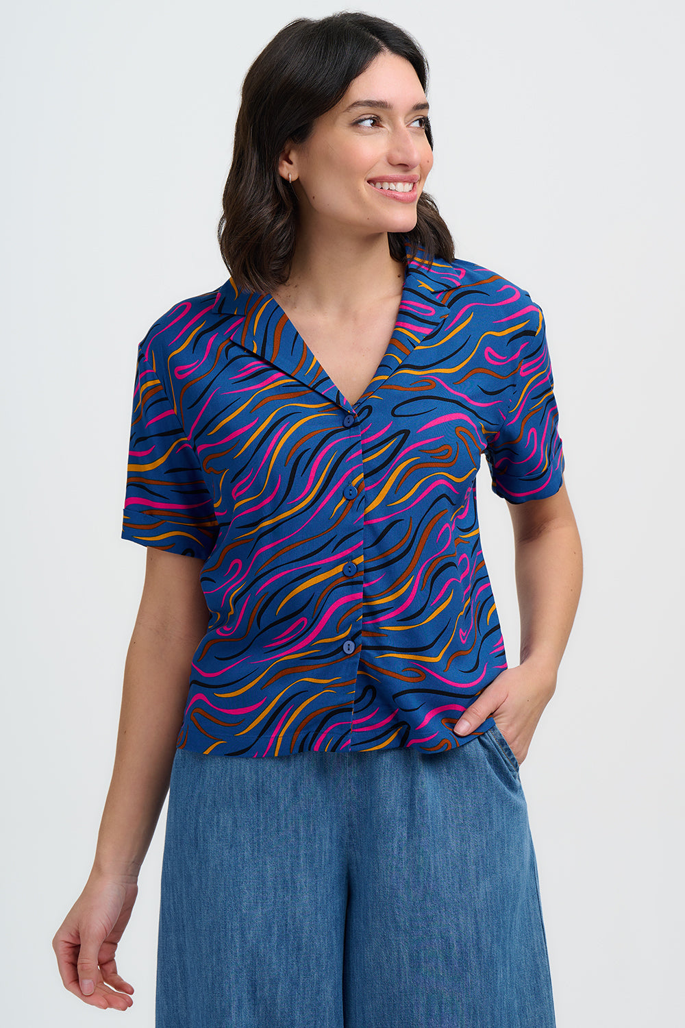 Woman wearing a colorful patterned shirt and blue pants on a white background