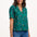 Sugarhill Brighton model wearing a green polka dot blouse and blue jeans on a white background