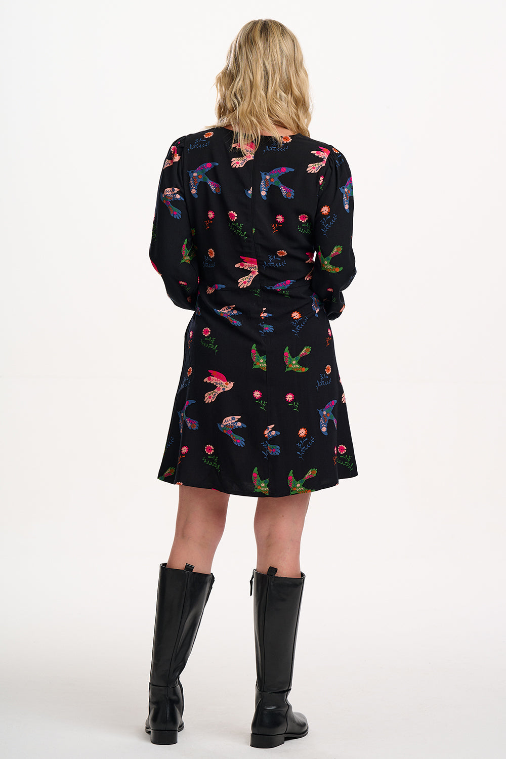 Sugarhill brighton model wearing a black dress with colourful floral patterns and black boots on a white background