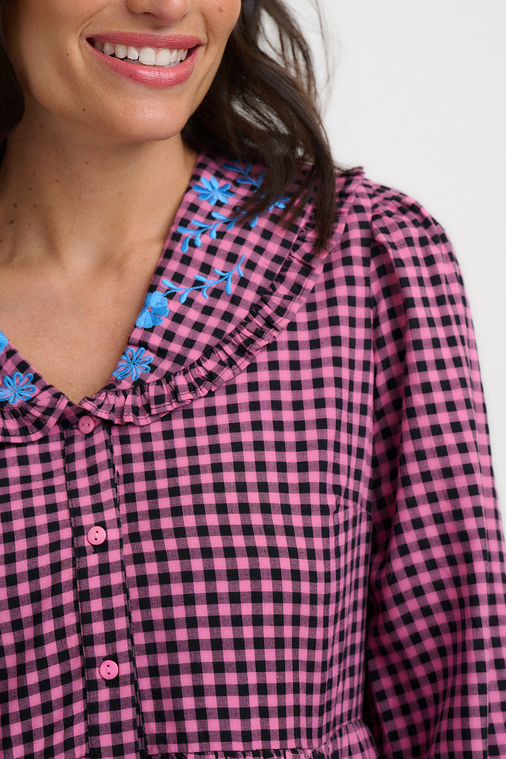 Close-up of a person wearing a pink and black checkered shirt with floral details.