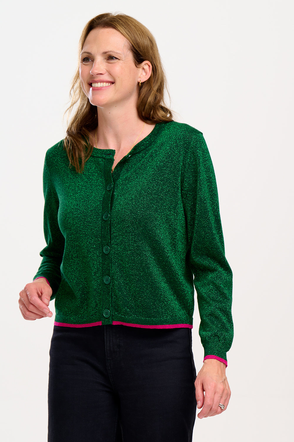 A woman smiling and wearing a green sparkle cardigan with a deep v neckline, ribbed cuffs, and pink stripes, over a dinosaur print top.