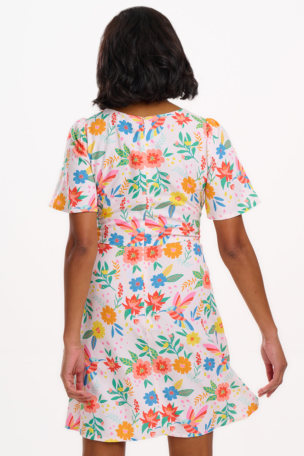 A woman wearing an off-white mini dress with a Tropical Hummingbird print, featuring fluted sleeves and a self-tie belt.