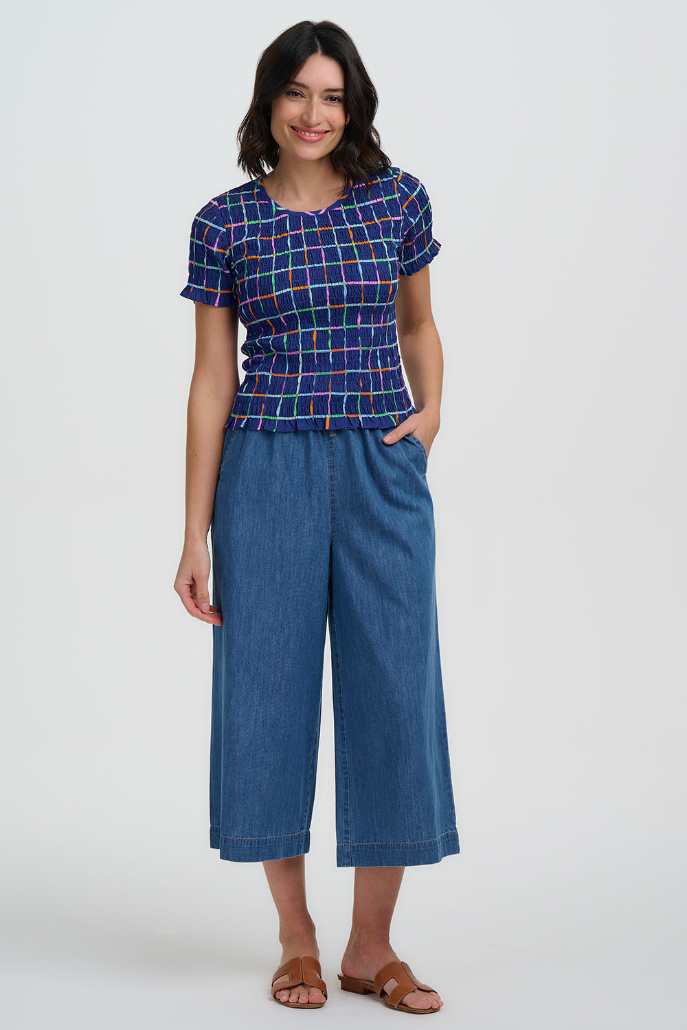 Woman wearing a blue plaid top and denim pants on a white background