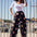 A model wearing black palazzo pants with a vibrant tropical parrots print, paired with a white top and accessories.