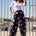 A model wearing black palazzo pants with a vibrant tropical parrots print, paired with a white top and accessories.