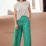 Woman wearing a white t-shirt and green patterned pants standing on a brick pavement.