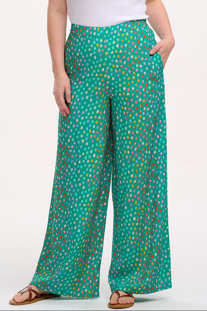 A woman modeling green palazzo pants with a multicolored dot pattern, paired with a white t-shirt.